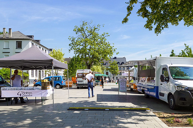 Blick über den sonnigen Marktplatz mit verschiedenen Marktständen und Foodtrucks.