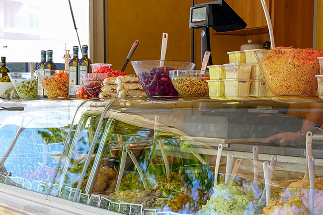 Nahaufnahme einer Theke mit einer großen Auswahl an bunten Antipasti, Salaten und gefüllten Teigtaschen in Glasschalen.