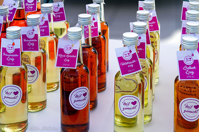 Viele kleine Glasflaschen mit verschiedenfarbigem Essig und Etiketten mit der Aufschrift „Mit Liebe gemacht“.