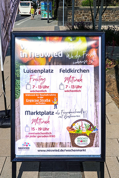 Ein Aufsteller mit einem Plakat, das die Termine für die Wochenmärkte in Neuwied ankündigt, inklusive des Feierabendmarktes am Mittwoch.