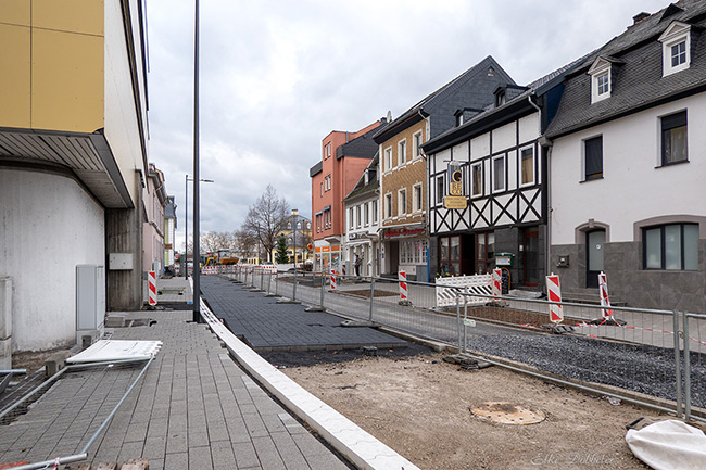 Perspektivische Ansicht der Baustelle in der Schlossstraße mit beidseitigen Absperrgittern, verschiedenen Geschäftsgebäuden und Blick in Richtung Marktplatz.