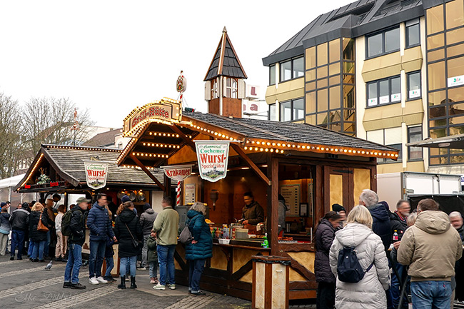Ein hölzerner Imbissstand mit der Aufschrift „Grill-Hütte“ und Schildern für Cochemer Wurstspezialitäten. Eine kleine Schlange von Menschen wartet vor dem beleuchteten Tresen. Foto: Elke Döbbeler