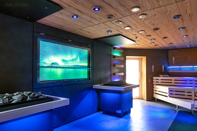 Die neue Sauna in stimmungsvolles blaues Licht getaucht. Im Hintergrund ein großer Bildschirm, der eine Polarlicht-Szene über einer Berglandschaft zeigt. Foto: Elke Döbbeler