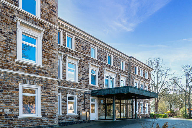 Die beeindruckende, mehrstöckige Steinfassade der Dr. von Ehrenwallschen Klinik mit weißen Fensterrahmen und einem großen, dunklen Vordach über dem Eingangsbereich.